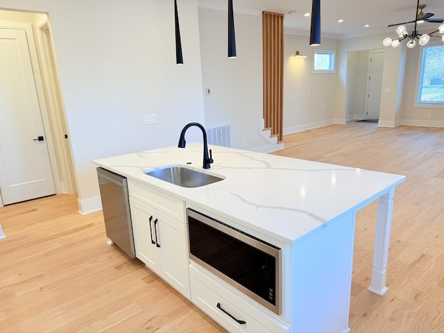 kitchen featuring sink, light stone counters, decorative light fixtures, appliances with stainless steel finishes, and a kitchen island with sink