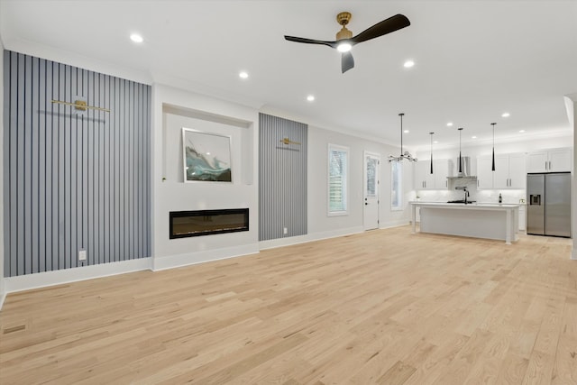 unfurnished living room with crown molding, light wood-style floors, a glass covered fireplace, a ceiling fan, and a sink