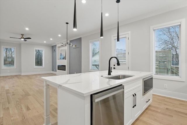 kitchen with a center island with sink, stainless steel appliances, ornamental molding, a glass covered fireplace, and a sink