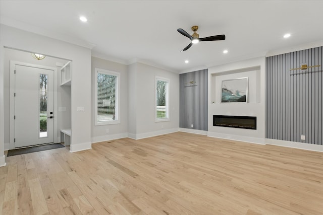 unfurnished living room with baseboards, a glass covered fireplace, crown molding, light wood-style floors, and recessed lighting