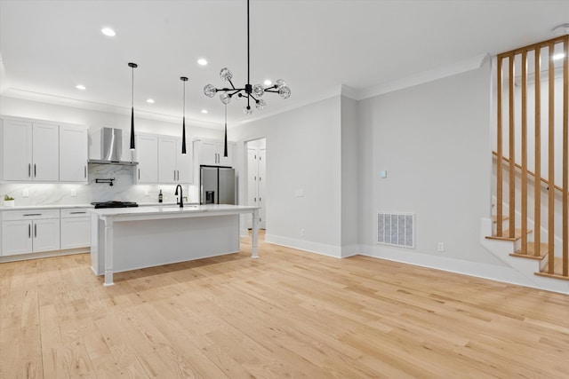 kitchen featuring visible vents, ornamental molding, light wood-type flooring, stainless steel fridge, and wall chimney exhaust hood