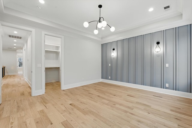 unfurnished room with light wood finished floors, a raised ceiling, visible vents, and an inviting chandelier