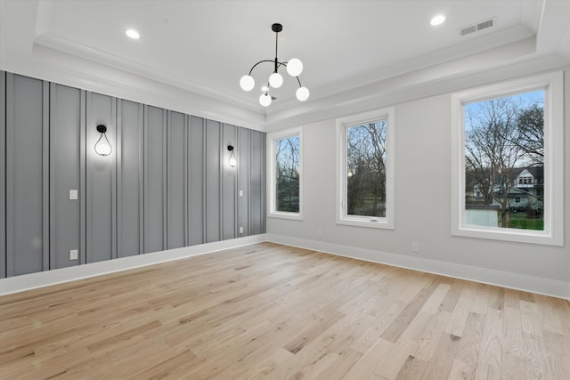 unfurnished room with light wood finished floors, a raised ceiling, visible vents, and baseboards