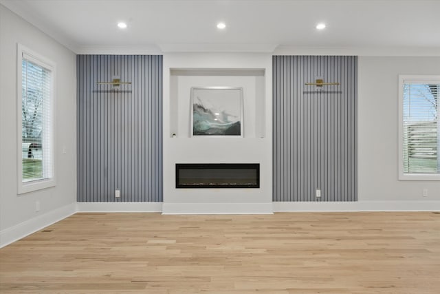 unfurnished living room with recessed lighting, light wood-style flooring, crown molding, and a glass covered fireplace