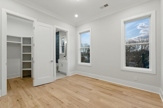 unfurnished bedroom featuring a walk in closet, visible vents, light wood-style flooring, ornamental molding, and baseboards