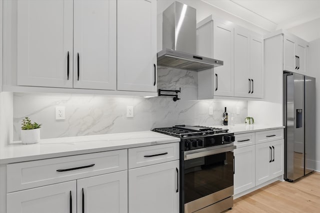 kitchen featuring backsplash, light wood-style flooring, appliances with stainless steel finishes, white cabinetry, and wall chimney exhaust hood