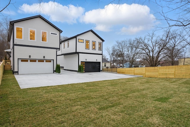 rear view of house with an attached garage, driveway, fence, and a lawn