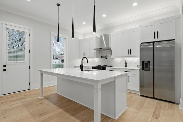 kitchen featuring stainless steel fridge with ice dispenser, wall chimney exhaust hood, light wood-style flooring, a kitchen island with sink, and backsplash