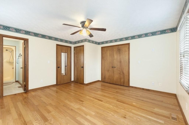 unfurnished bedroom featuring ceiling fan, ensuite bath, light hardwood / wood-style floors, and multiple closets