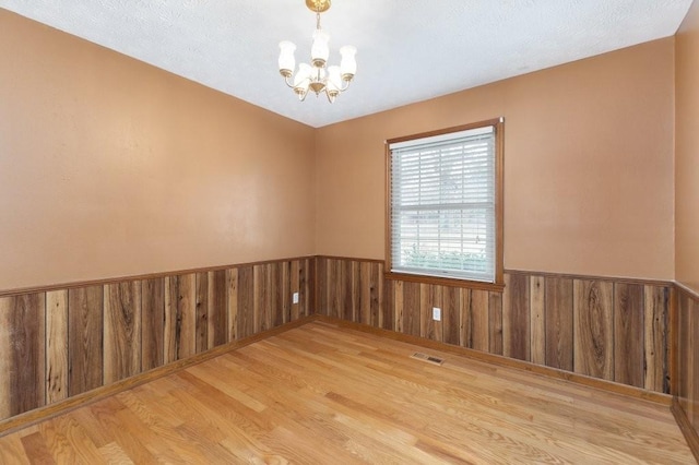 unfurnished room with wooden walls, a notable chandelier, and light wood-type flooring