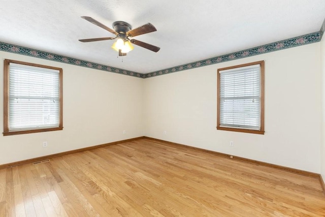 empty room with ceiling fan, a wealth of natural light, and light hardwood / wood-style floors