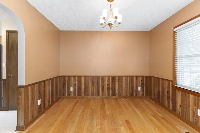 unfurnished room with an inviting chandelier, light hardwood / wood-style floors, a textured ceiling, and wood walls