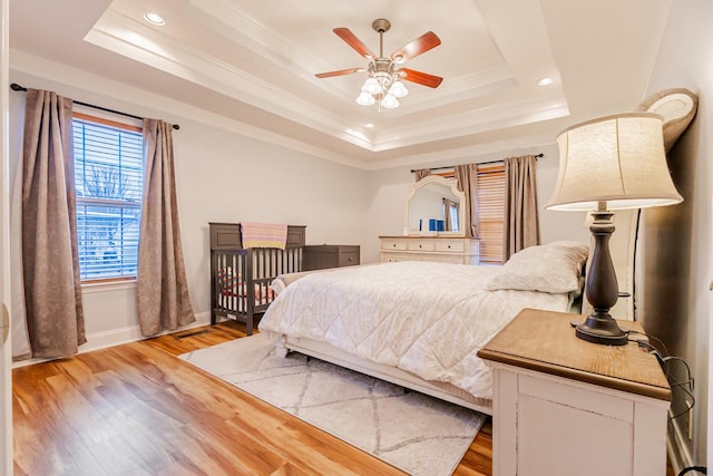 bedroom with ornamental molding, light hardwood / wood-style floors, and a tray ceiling