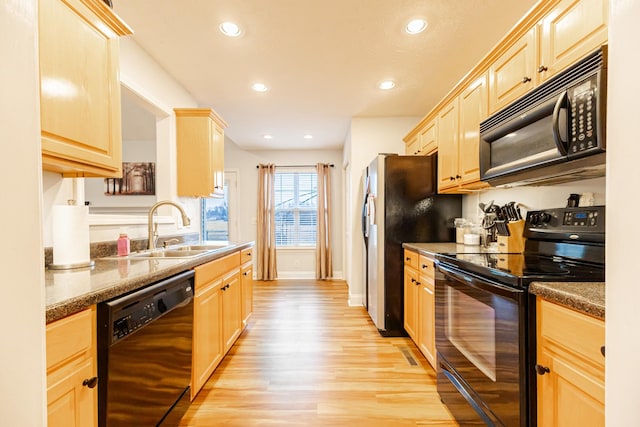 kitchen with sink, dark stone countertops, light wood-type flooring, and black appliances