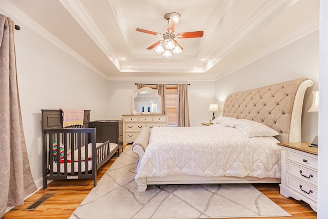 bedroom featuring crown molding, light hardwood / wood-style floors, a raised ceiling, and ceiling fan