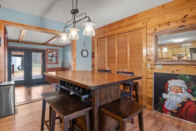 dining space with french doors, light hardwood / wood-style floors, and wood walls