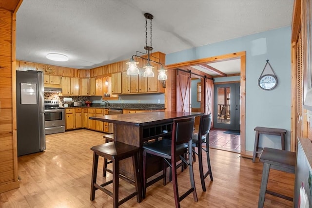 kitchen featuring stainless steel appliances, light hardwood / wood-style flooring, a textured ceiling, and decorative light fixtures