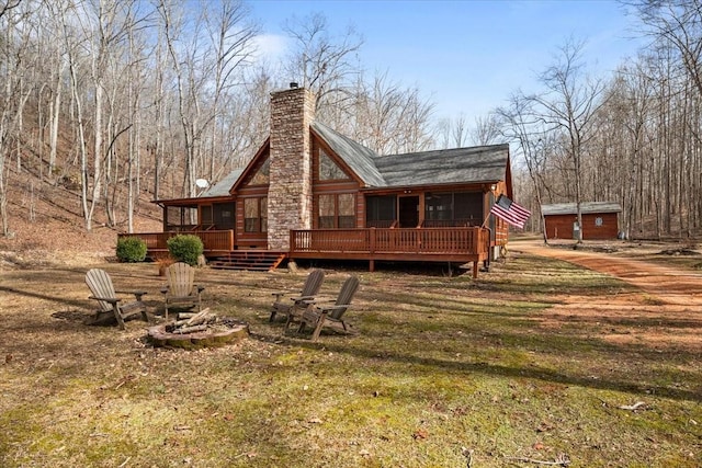 back of house with a fire pit, a sunroom, a storage unit, and a deck