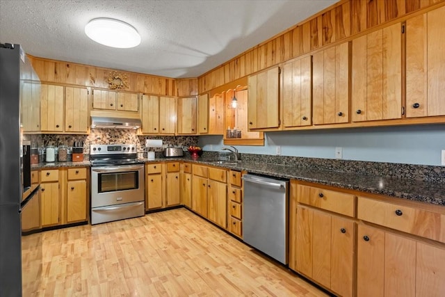 kitchen with sink, a textured ceiling, light hardwood / wood-style flooring, dark stone countertops, and stainless steel appliances