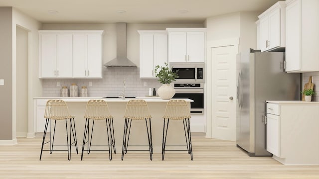 kitchen featuring wall chimney exhaust hood, tasteful backsplash, an island with sink, stainless steel appliances, and white cabinets