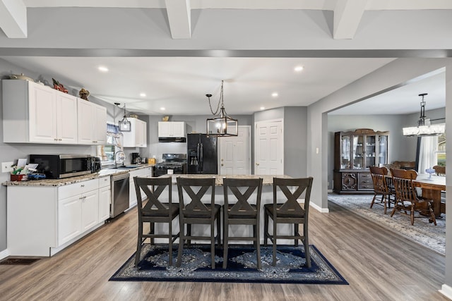 kitchen featuring white cabinets, a kitchen island, light stone counters, and black appliances