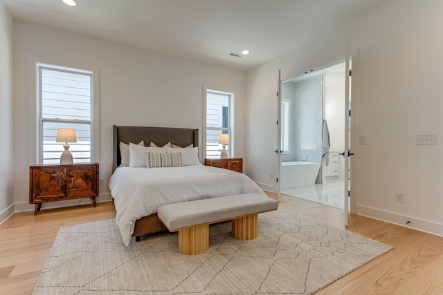 bedroom featuring multiple windows, connected bathroom, and light wood-type flooring