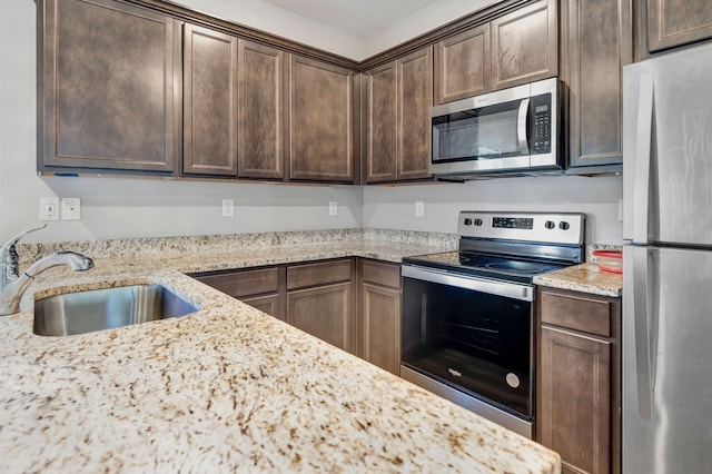 kitchen featuring dark brown cabinetry, sink, light stone countertops, and appliances with stainless steel finishes