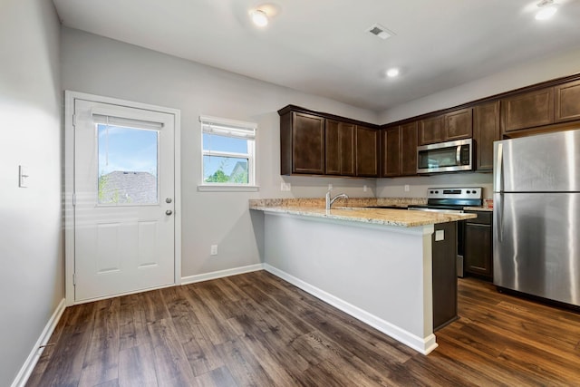 kitchen featuring dark wood-type flooring, light stone counters, dark brown cabinets, kitchen peninsula, and stainless steel appliances