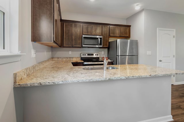 kitchen featuring appliances with stainless steel finishes, dark brown cabinetry, kitchen peninsula, light stone countertops, and dark wood-type flooring