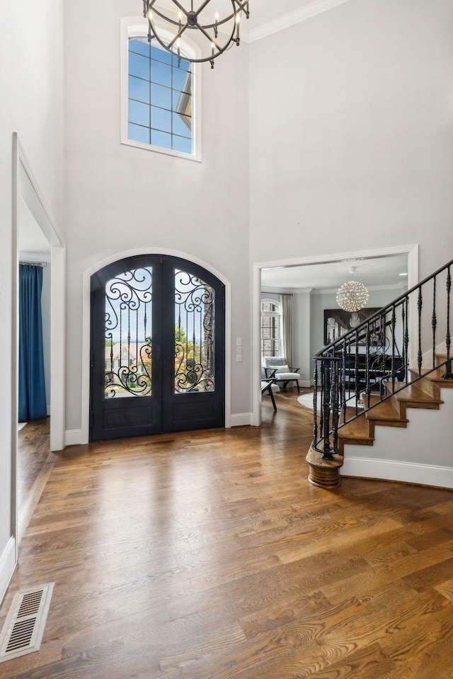 foyer entrance featuring french doors, ornamental molding, a notable chandelier, hardwood / wood-style flooring, and a high ceiling