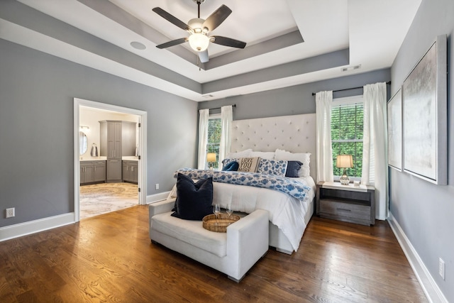 bedroom featuring ensuite bathroom, dark hardwood / wood-style floors, ceiling fan, and a tray ceiling