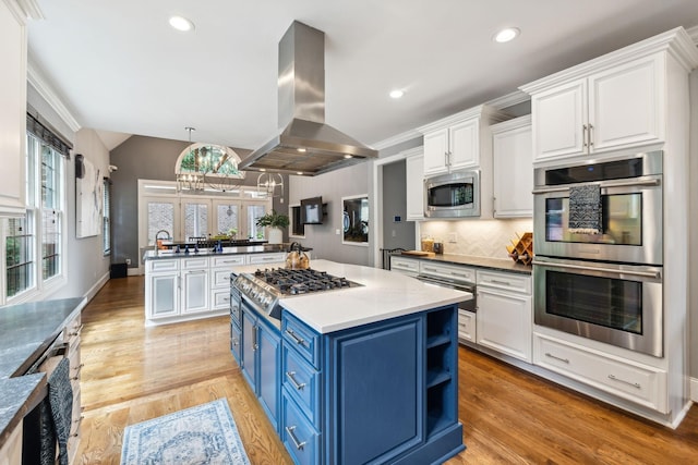 kitchen featuring pendant lighting, appliances with stainless steel finishes, blue cabinets, light hardwood / wood-style floors, and island exhaust hood