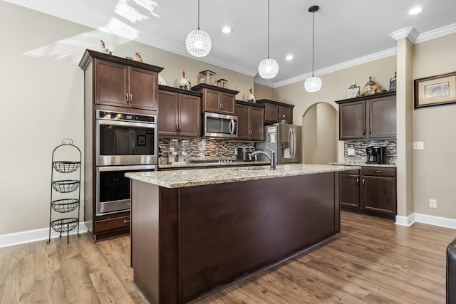 kitchen with dark brown cabinetry, light stone counters, decorative light fixtures, a center island with sink, and stainless steel appliances