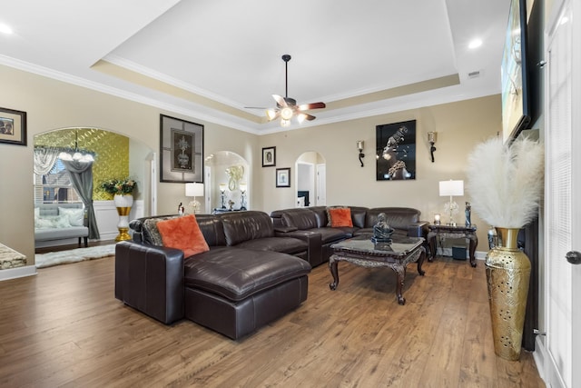 living room with a raised ceiling, ornamental molding, hardwood / wood-style floors, and ceiling fan