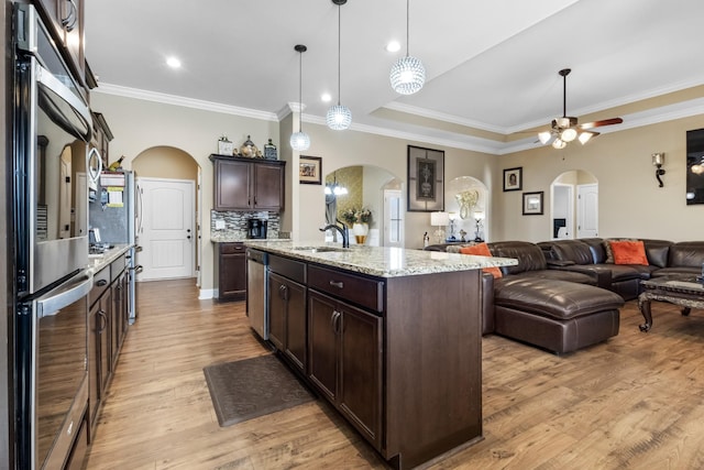 kitchen with an island with sink, sink, hanging light fixtures, fridge, and dark brown cabinetry