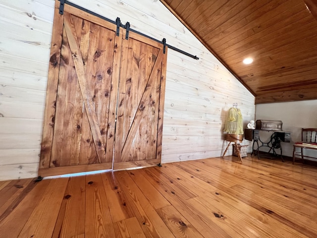 additional living space with hardwood / wood-style flooring, wooden walls, vaulted ceiling, wooden ceiling, and a barn door