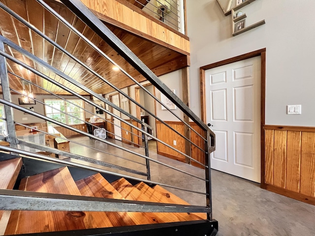 stairs with wooden ceiling, concrete floors, and wood walls