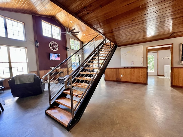 staircase featuring a towering ceiling, wooden walls, concrete flooring, washer / clothes dryer, and wooden ceiling