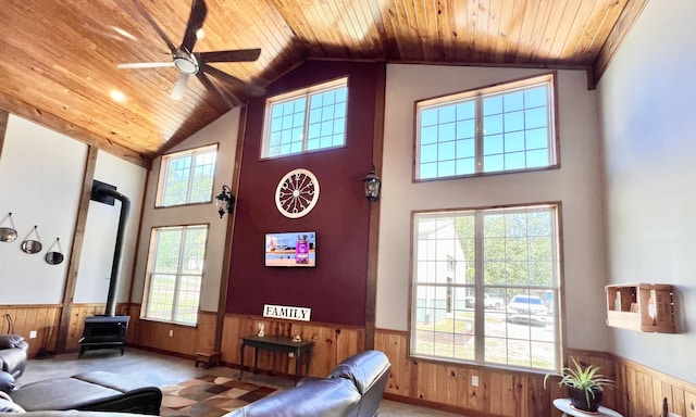 living room featuring a wood stove, ceiling fan, high vaulted ceiling, wooden ceiling, and wood walls