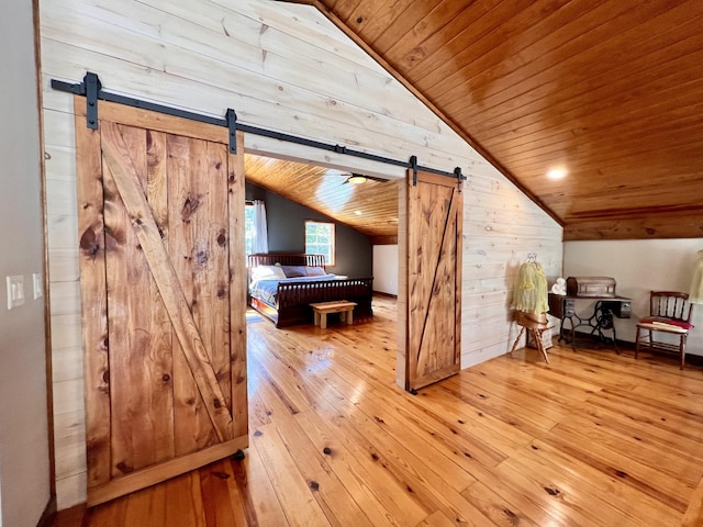 interior space with vaulted ceiling, wooden walls, wood ceiling, a barn door, and light hardwood / wood-style flooring