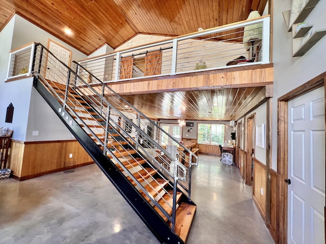 staircase featuring concrete flooring, high vaulted ceiling, wooden ceiling, and wood walls