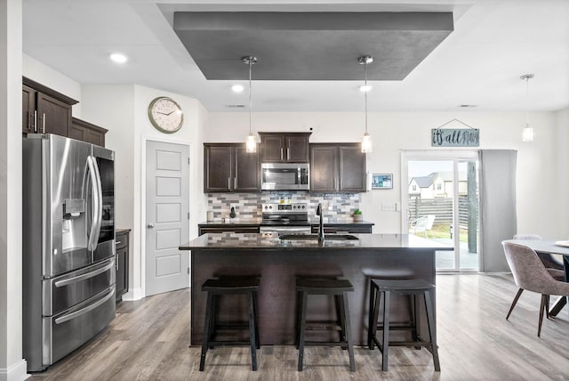 kitchen with sink, pendant lighting, stainless steel appliances, a kitchen island with sink, and decorative backsplash