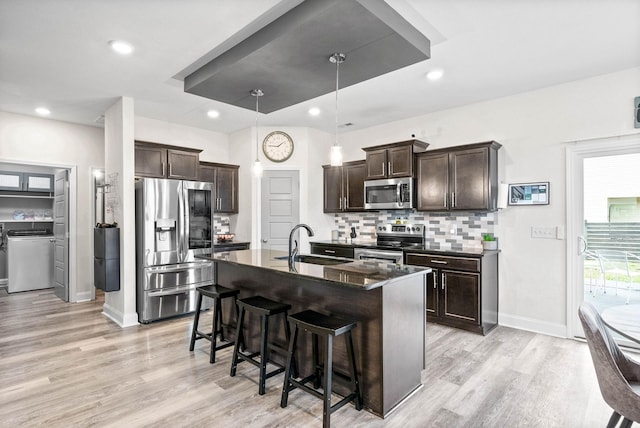 kitchen featuring sink, light wood-type flooring, stainless steel appliances, a kitchen island with sink, and backsplash