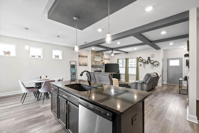 kitchen featuring stainless steel dishwasher, decorative light fixtures, a kitchen island with sink, and sink