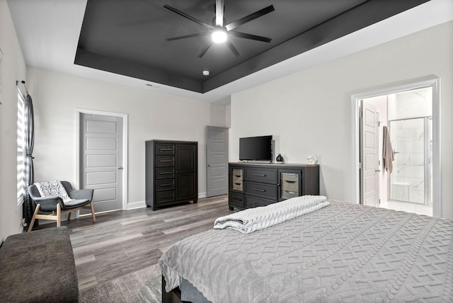 bedroom with ceiling fan, connected bathroom, a tray ceiling, and light hardwood / wood-style flooring