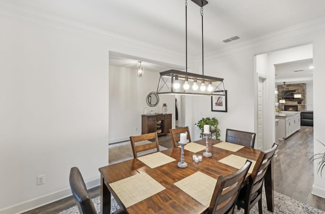 dining room featuring crown molding, a stone fireplace, and dark wood-type flooring