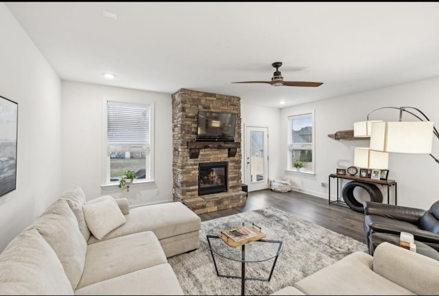 living room featuring dark hardwood / wood-style floors, ceiling fan, and a stone fireplace