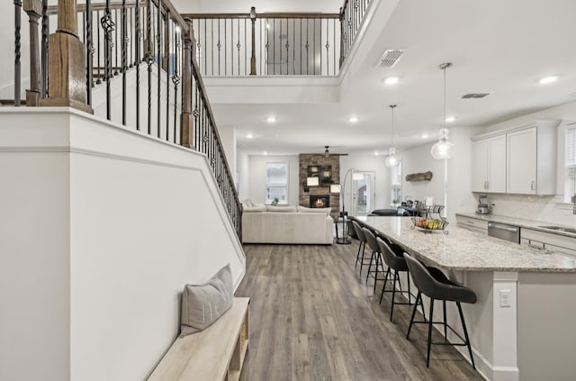 kitchen featuring a fireplace, decorative light fixtures, a breakfast bar area, white cabinets, and hardwood / wood-style flooring