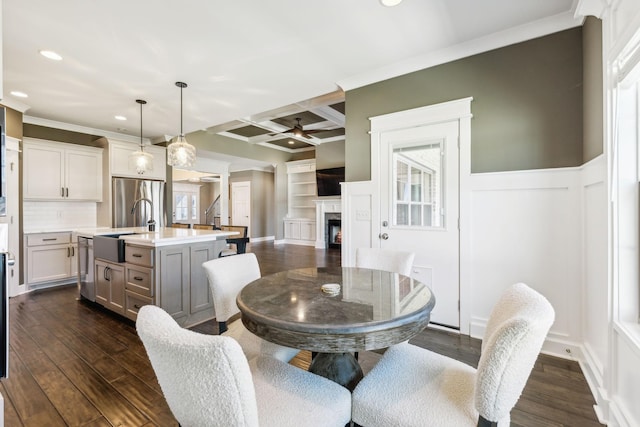 dining area featuring dark hardwood / wood-style floors, beamed ceiling, sink, coffered ceiling, and ceiling fan