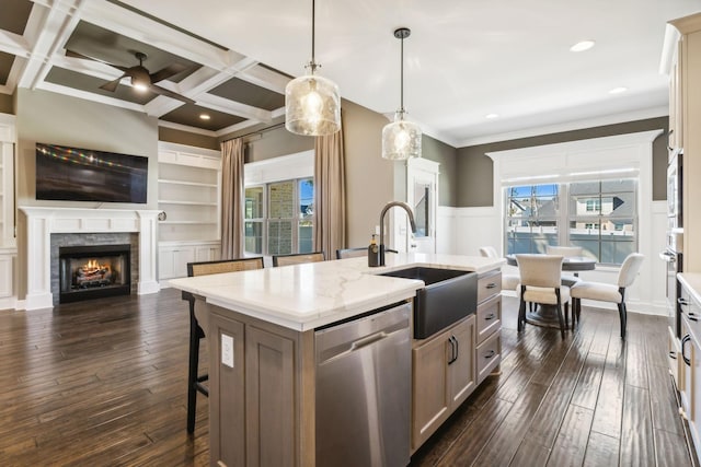 kitchen with pendant lighting, sink, coffered ceiling, a kitchen island with sink, and stainless steel dishwasher